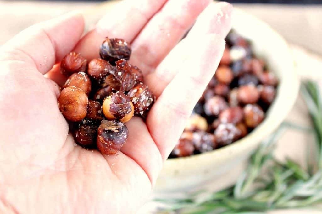 Move over popcorn; there's a new snack kid in town! Roasted Rosemary Hazelnuts (a.k.a. filberts) are as addicting as popcorn. And they're good for you too. | Kudos Kitchen by Renee A closeup photo of a hand holding a bunch of Skillet Roasted Rosemary Hazelnuts