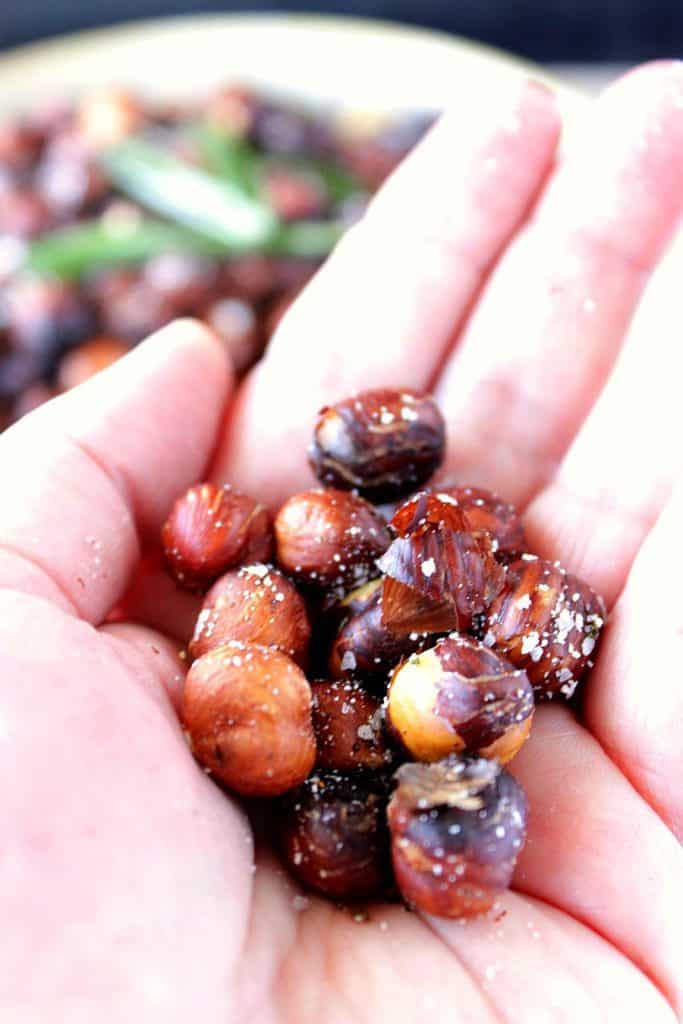 A closeup of a hand holding a palm-full of Skillet Roasted Rosemary Hazelnuts