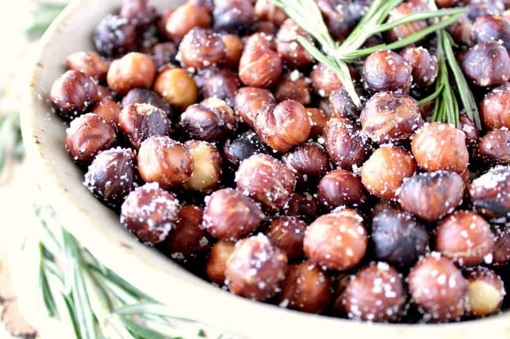 An offset closeup horizontal photo of a bowl filled with Skillet Roasted Rosemary Hazelnuts