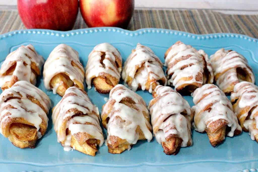 A horizontal photo of a blue plate of apple pie wedges with icing.