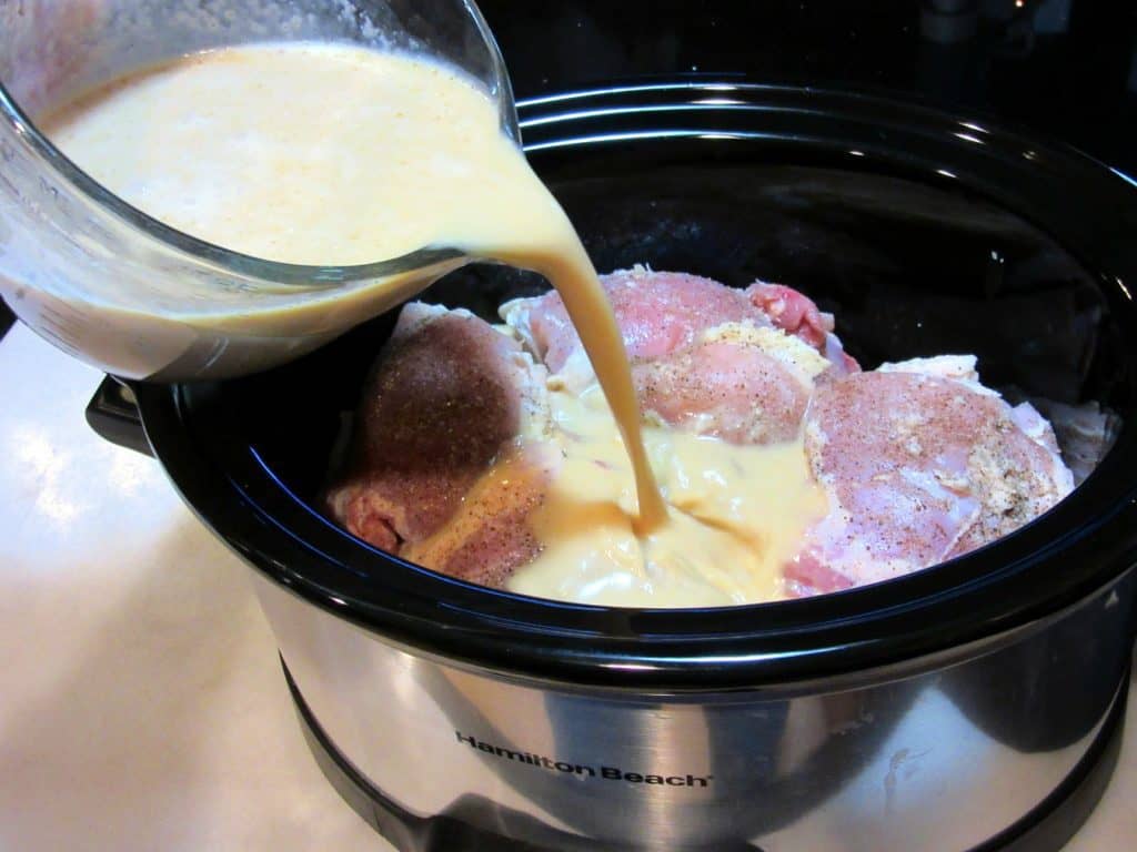 Coconut milk being poured over chicken thighs.