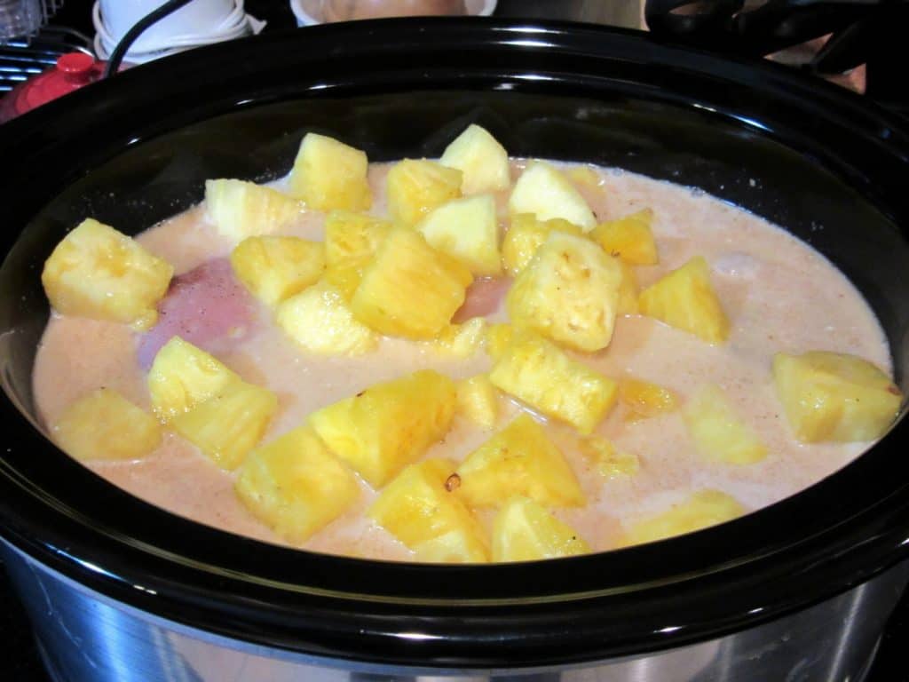 Pineapple chunks added to a slow cooker.