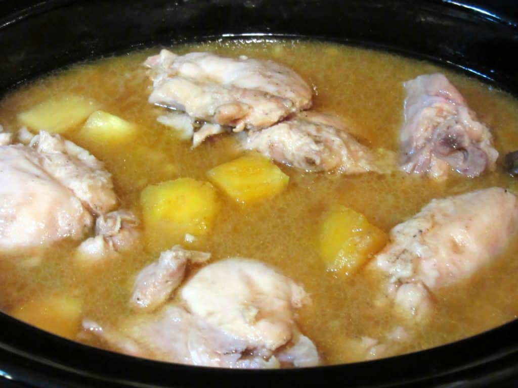 Cooked chicken thighs in pineapple liquid in a slow cooker.