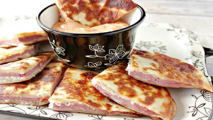A tray of Rueben Quesadillas and some dipping sauce surrounded by a black and white napkin.