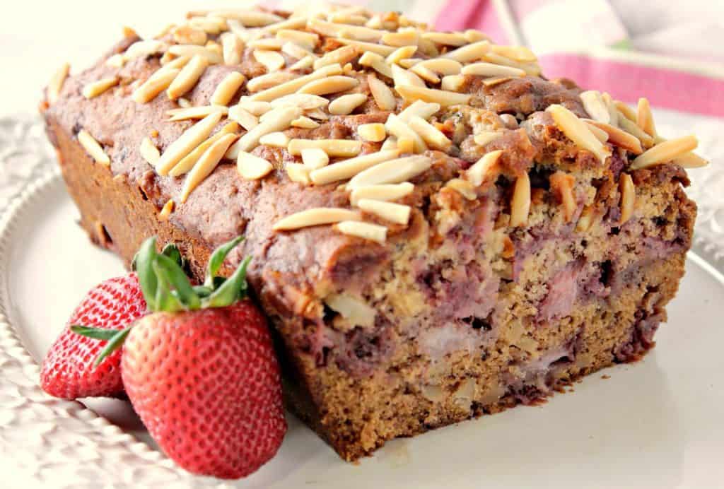 Strawberry Banana Bread on a platter  with strawberries and almonds as garnish.
