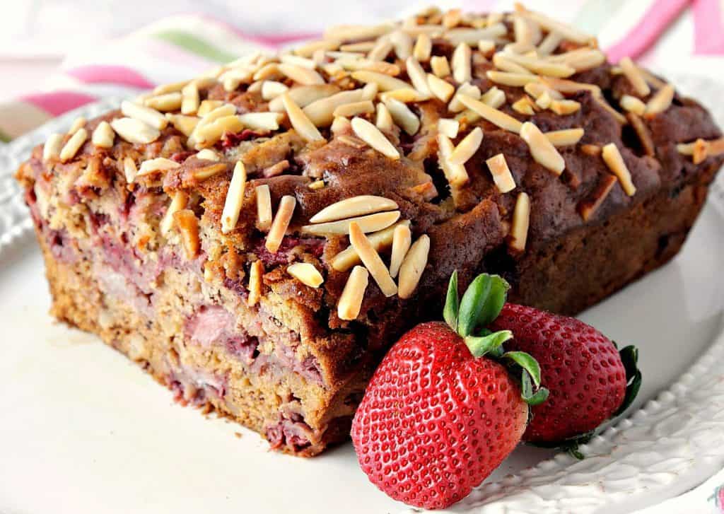 Strawberry Banana Bread on a plate with fresh strawberries and almond slices.