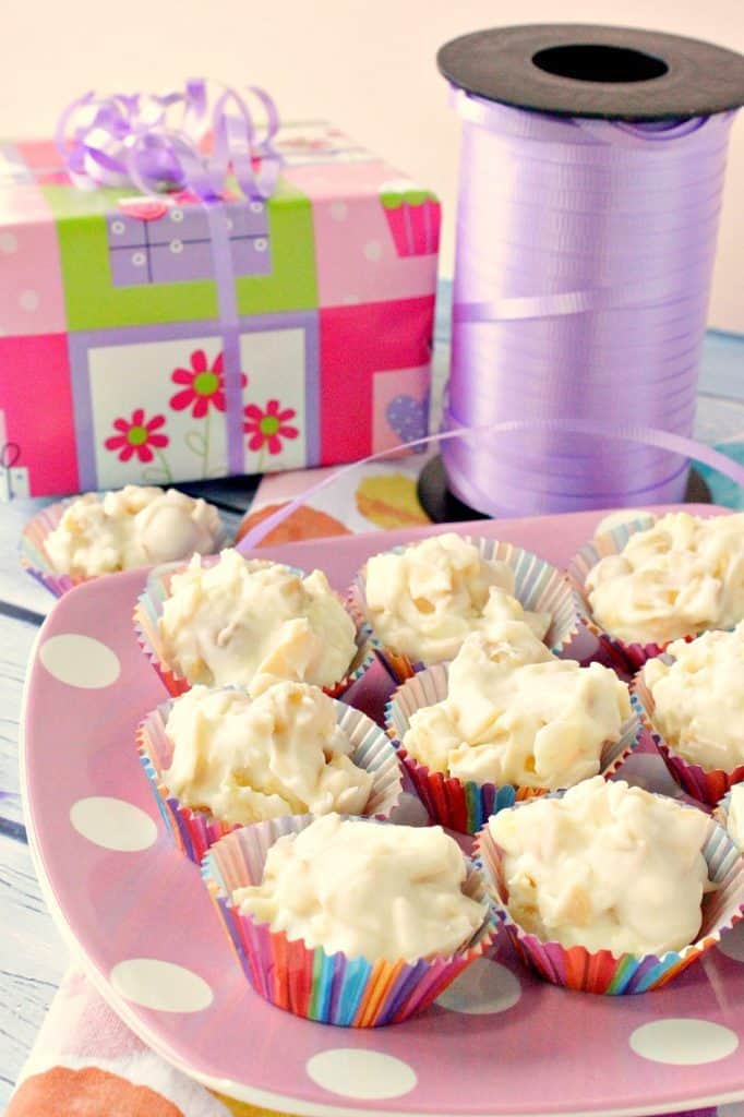 A vertical photo of a plate of tropical white chocolate candy with a gift wrapped package and a roll of ribbon in the background.