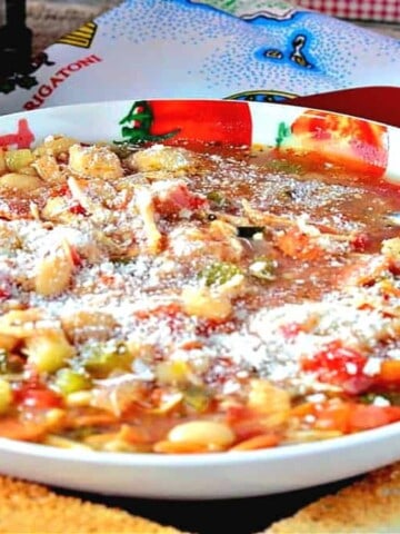 A bowl filled with Italian Pepperoni Soup with a spoon and toast slices in the foreground