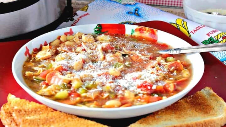 A bowl filled with Italian Pepperoni Soup with a spoon and toast slices in the foreground