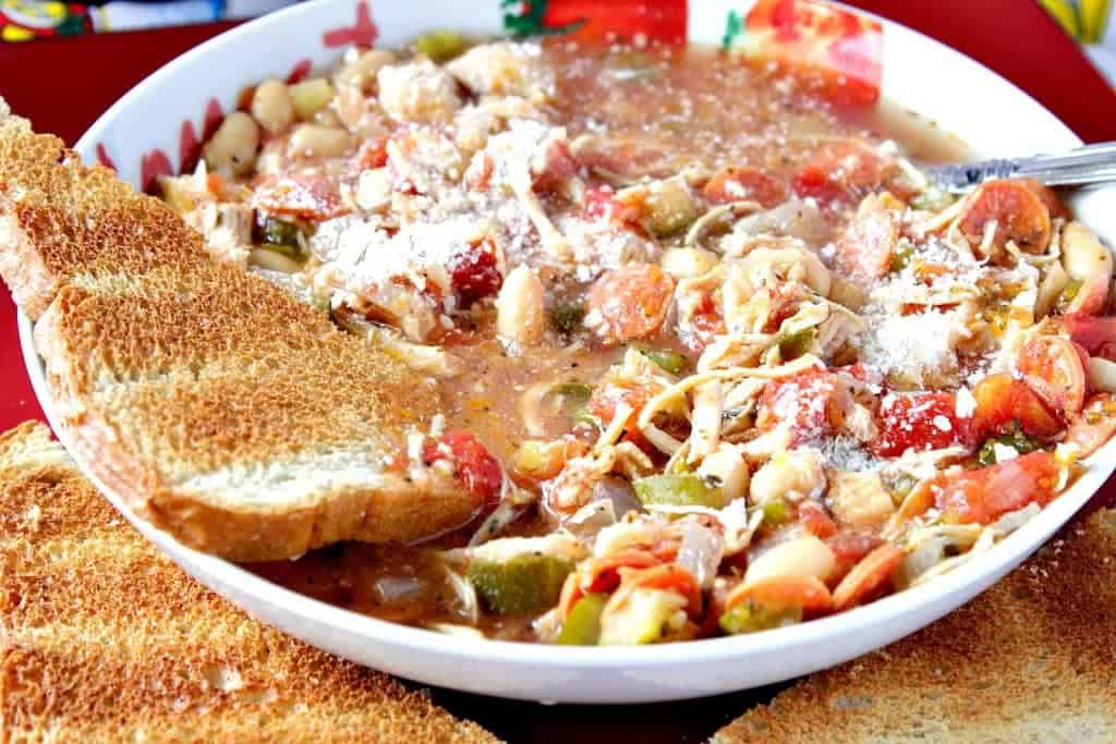 A closeup photo of Italian Pepperoni Soup in a bowl with a spoon and a piece of toast.