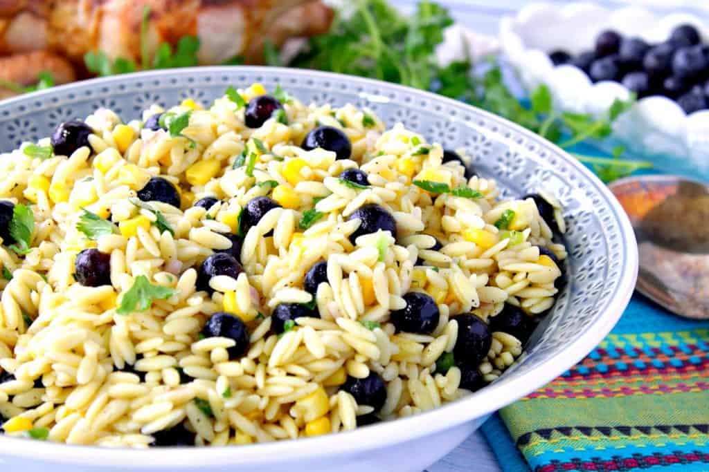 A blue bowl filled with Orzo Pasta Salad with blueberries and corn.