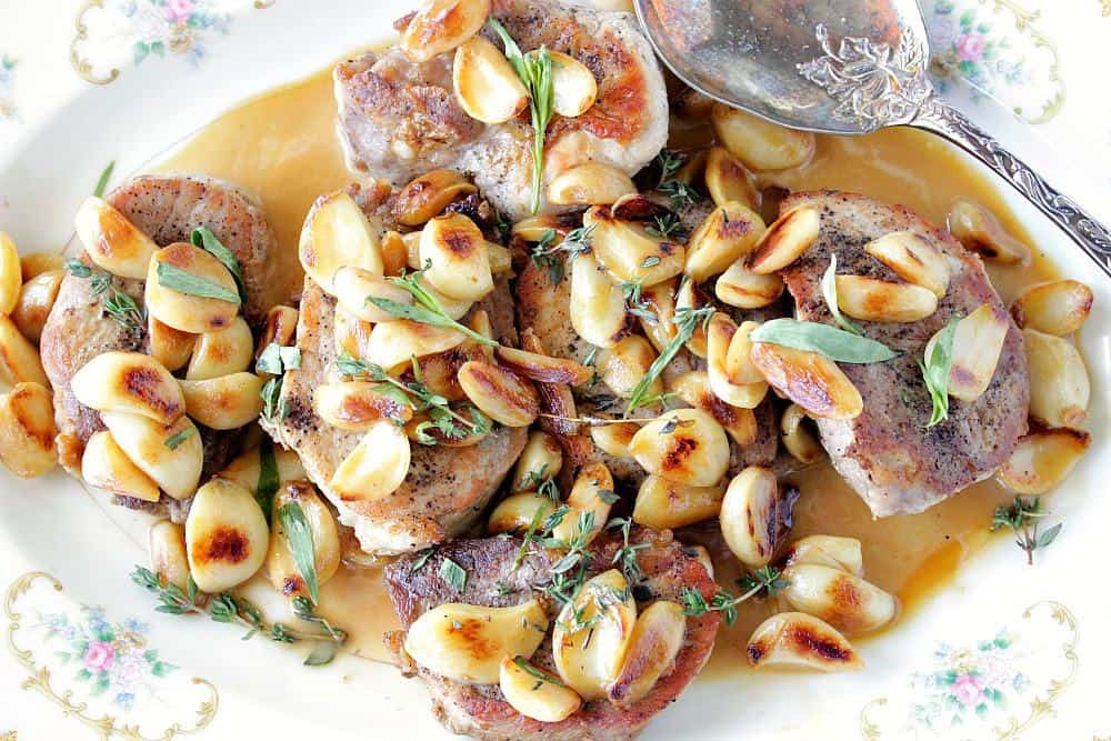 Overhead picture of garlic lovers pork chops on a platter with sage and herbs.