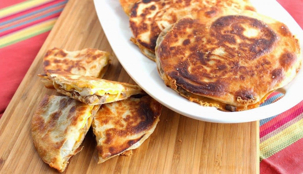 Overhead photo of a plate of breakfast quesadillas on a wood platter and a colorful Mexican napkin.