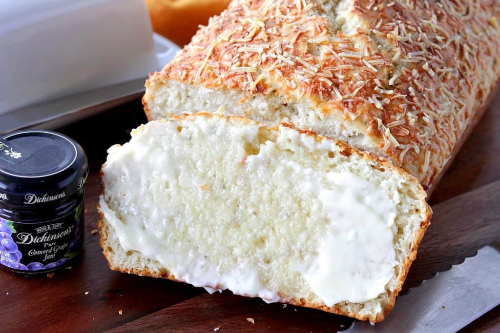 Slice of Herb Parmesan Savory Quick Bread with melted butter and a serrated knife.