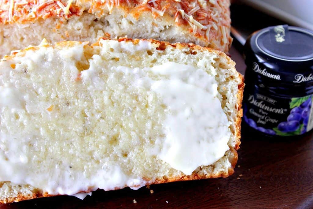 Closeup shot of Savory Parmesan Quick Bread with melted butter and a jar of jam.