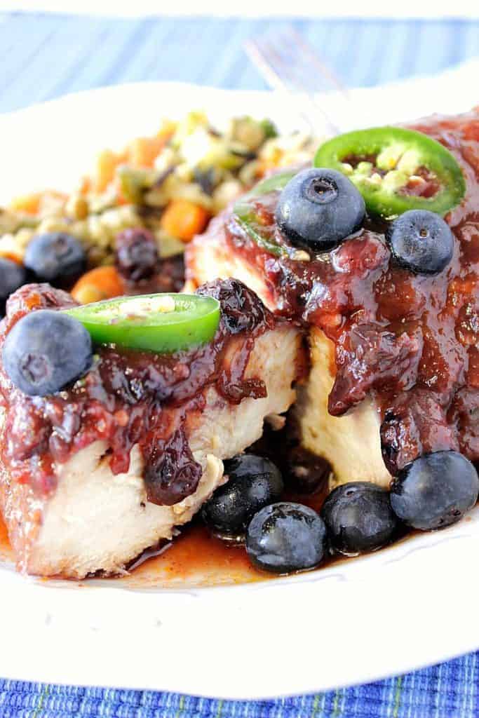 Closeup photo of the inside of a cooked chicken breast with blueberry bbq sauce, blueberries and green chile slices.