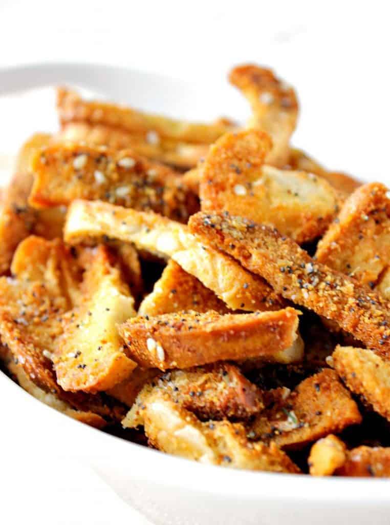 A closeup vertical photo of a bowl filled with golden brown and crunchy everything bagel chips.