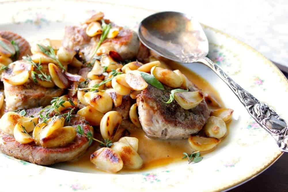 A horizontal photo of a platter of garlic lovers pork chops with fresh herbs and a serving spoon.