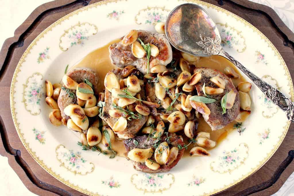 Overhead photo of a pretty platter of garlic lovers pork chops with a wooden charger, and a large serving spoon.