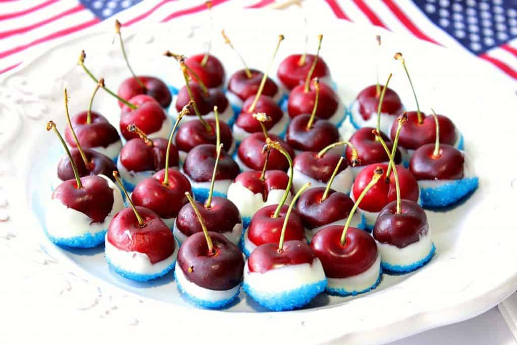 Red White and Blue Sugared Cherries on a white plate with flags in the background