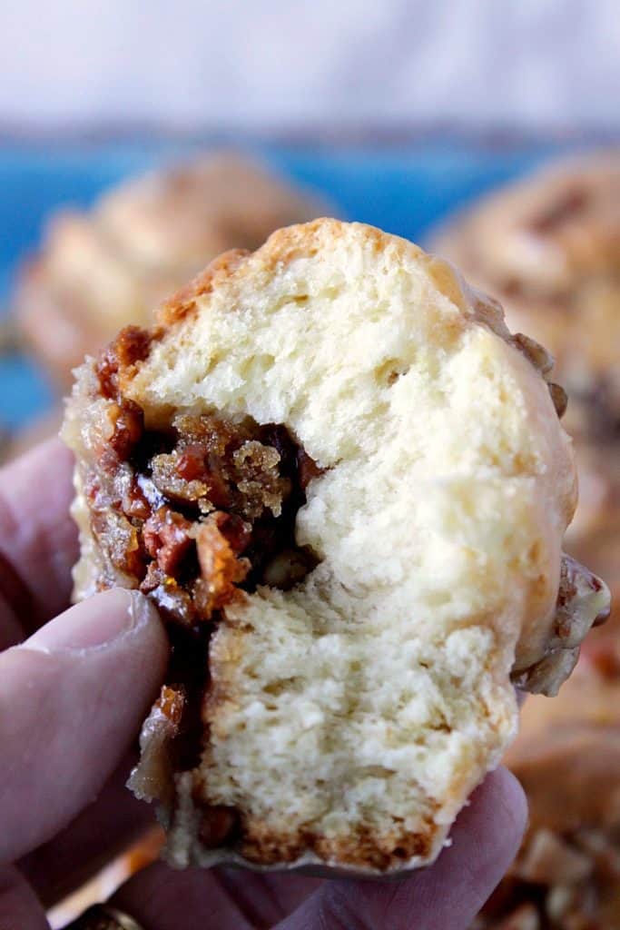 Close up picture of a hand holding a sticky caramel sweet roll with pecans