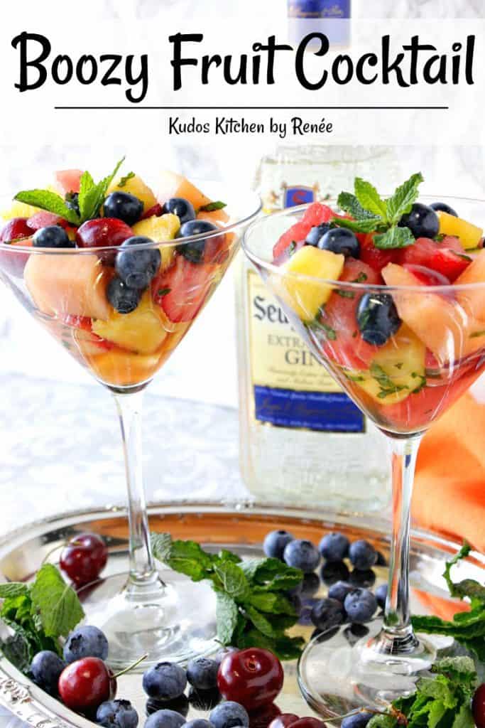 Two colorful Boozy Fruit Cocktails served in martini glasses with a bottle of gin in the background.