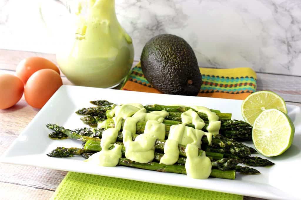 A white rectangle platter filled with roasted asparagus with avocado hollandaise sauce over top.