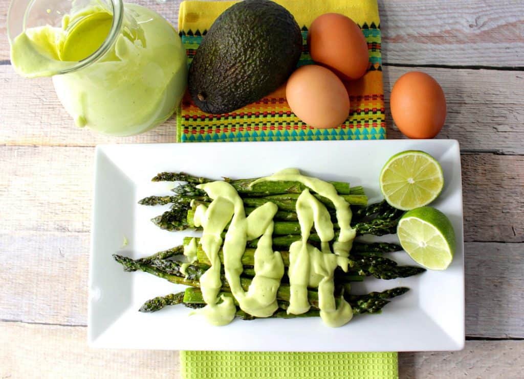 Overhead photo of a plate of roasted asparagus topped with avocado hollandaise sauce.