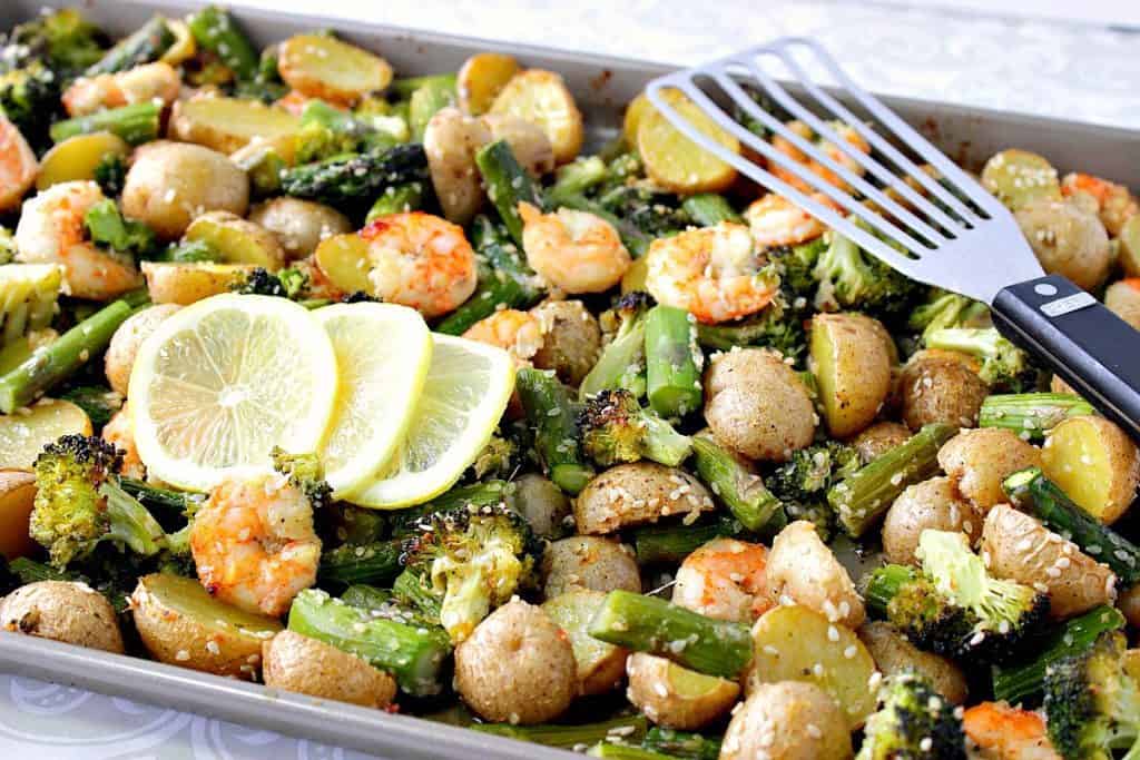 A sheet pan supper of Lemon Ginger Shrimp along with lemon slices and a slotted spatula.