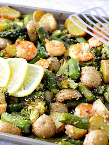 A sheet pan supper of Lemon Ginger Shrimp along with lemon slices and a slotted spatula.