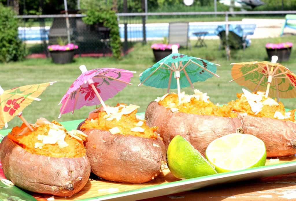 Outside photo of sweet potatoes on a tropical platter with paper umbrellas and a swimming pool in the background.