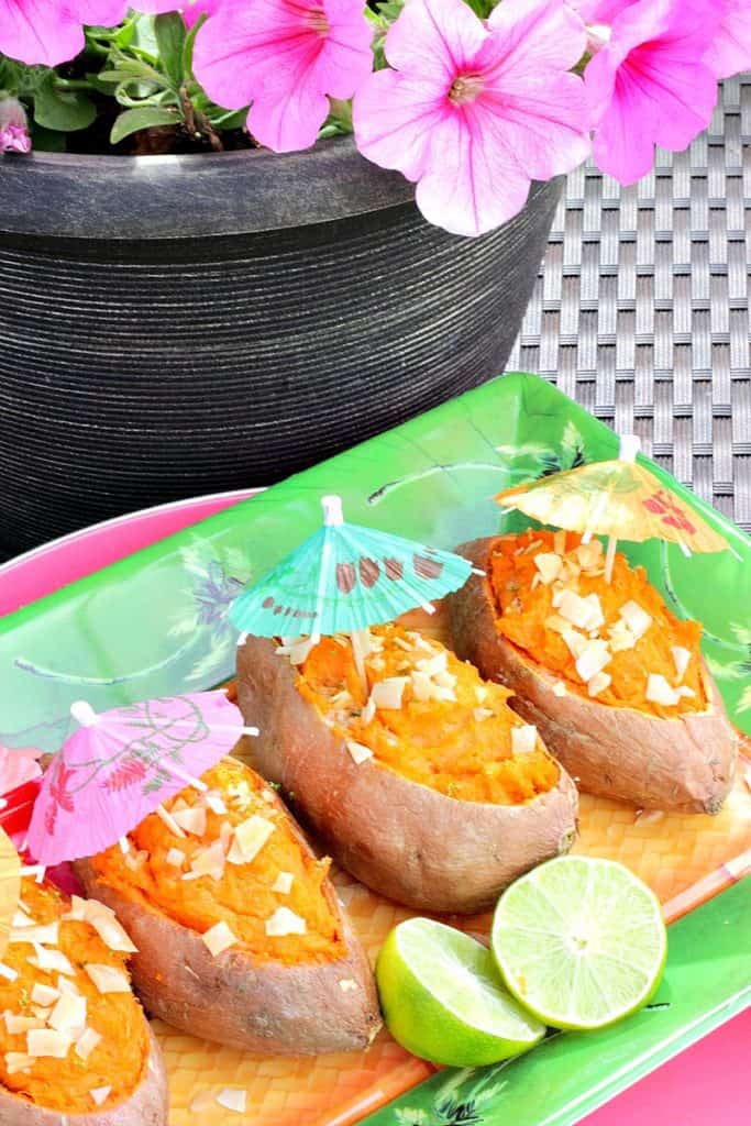 Tropical Twice Baked Sweet Potatoes Pink petunias in the background with sweet potatoes and paper umbrellas on a tropical plate.
