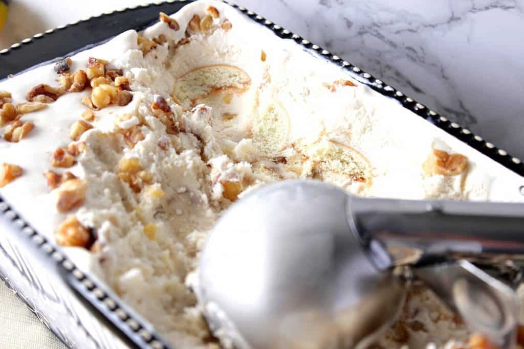 An ice cream scoop in a container of banana walnut ice cream