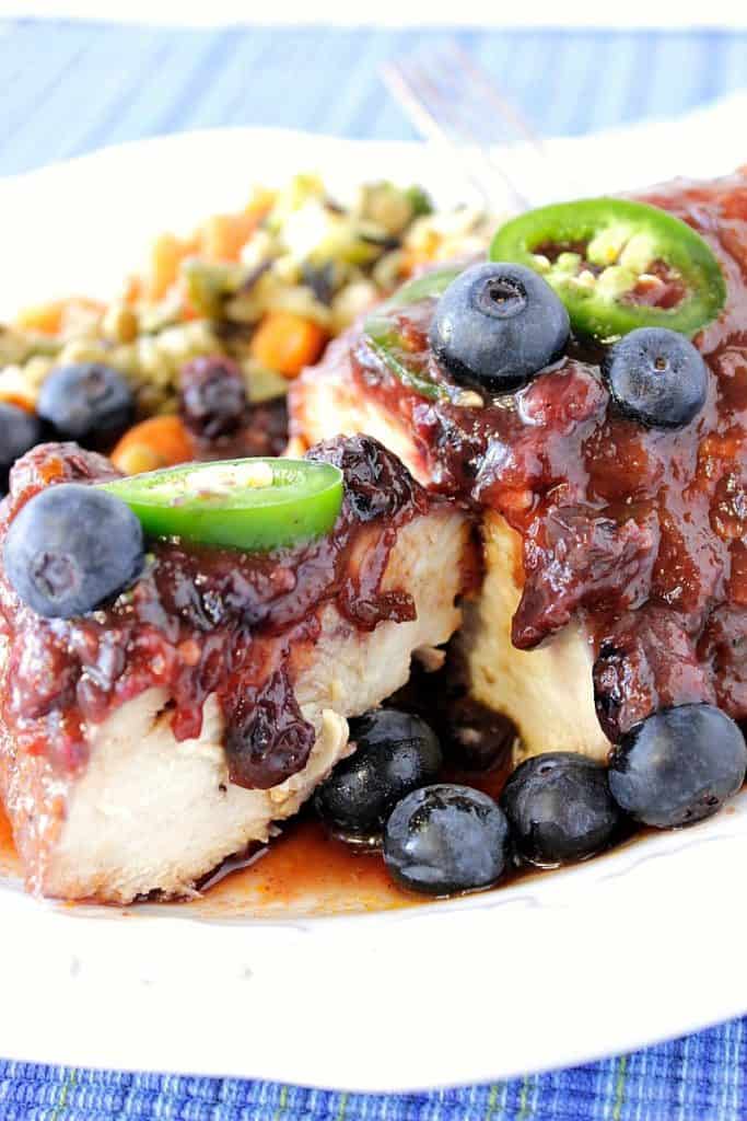 Closeup photo of a chicken breast on a white plate the blueberry BBQ sauce and sliced jalapenos.
