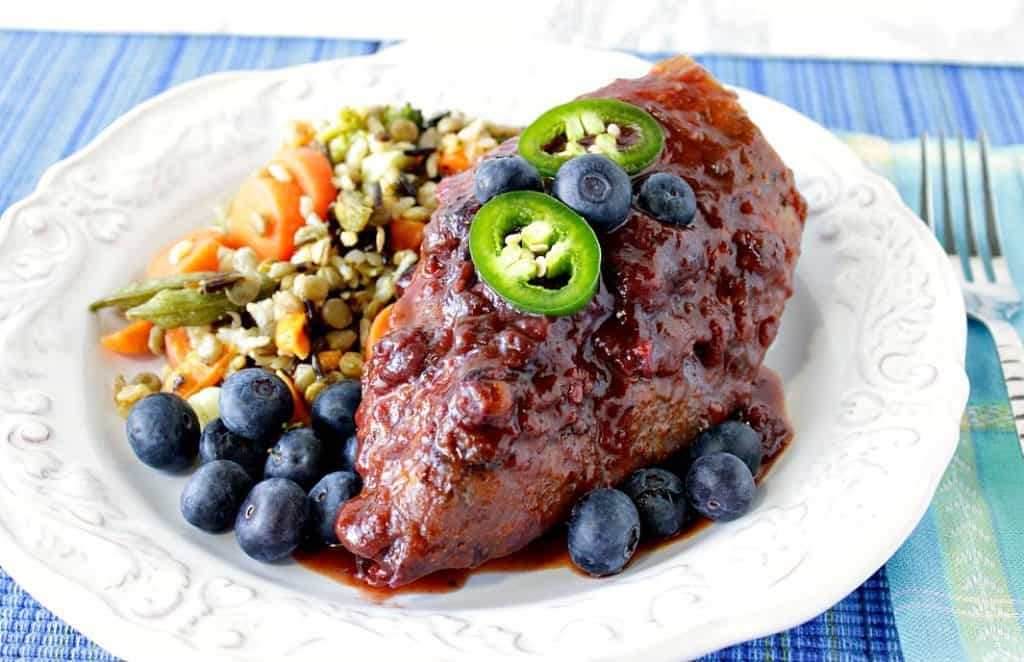 Blueberry BBQ Chicken breast on a white plate with a blue napkin, fresh blueberries, and jalapeno slices.