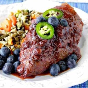 A Blueberry Chili Chicken Breast topped with jalapeno slices and blueberries on a plate.