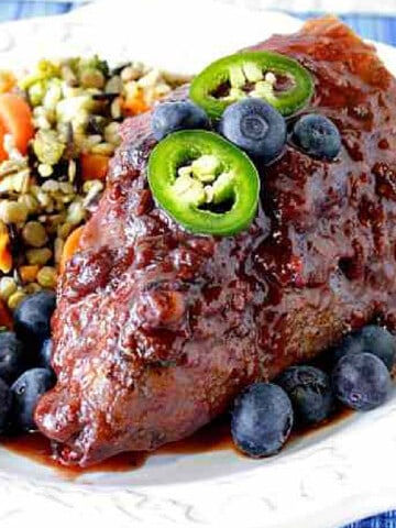 A Blueberry Chili Chicken Breast topped with jalapeno slices and blueberries on a plate.