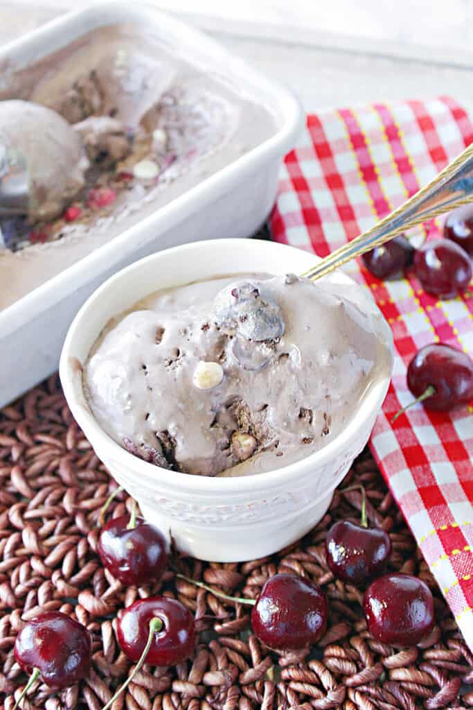 A vertical closeup image of a small dish filled with Chocolate Cherry Kahlua Ice cream with a spoon and a red and white napkin on the side.