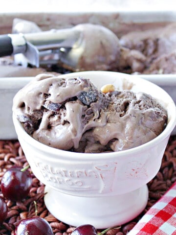 A dish of Chocolate Cherry Kahlua Ice Cream with cherries on the side along with a spoon and a red and white check napkin.