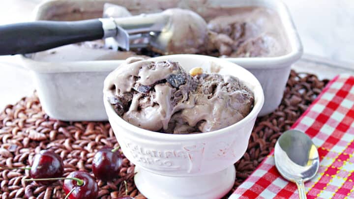 A dish of Chocolate Cherry Kahlua Ice Cream with cherries on the side along with a spoon and a red and white check napkin.