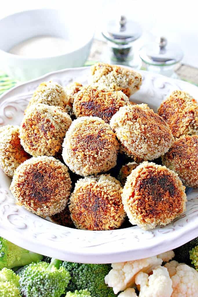 A vertical closeup of a white bowl filled with golden brown Broccoli Cauliflower Vegetable Tots along with a salt and pepper shaker in the background.