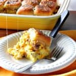 A breakfast slider with scrambled eggs and sausage on a white plate with a casserole dish in the background.