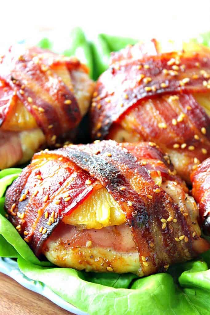 Closeup vertical photo of an easy chicken dinner of bacon wrapped teriyaki pineapple chicken thighs with sesame seeds on top on butter lettuce.