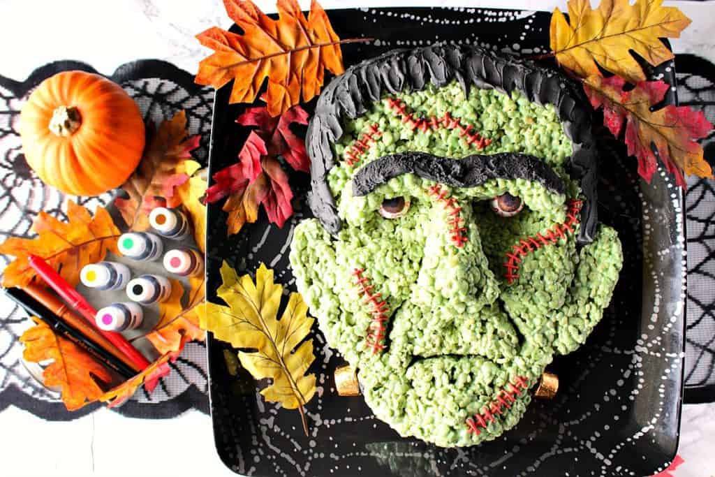 Overhead photo of a Frankenstein Rice Krispie Treat with gumball eyeballs on a platter with fall leaves.
