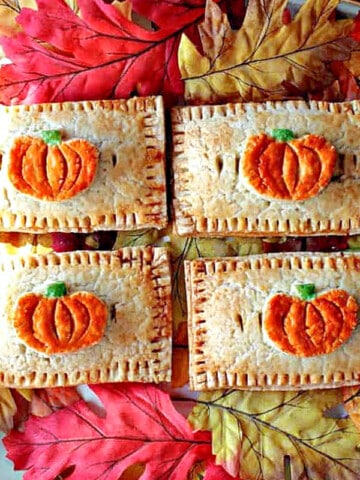 A direct overhead horizontal photo of four Pumpkin Hand Pies on a platter with autumn leaves surrounding the pies.