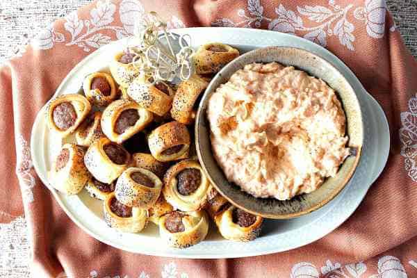 Overhead closeup image of a pile of brat bite appetizers with poppy seeds and sauerkraut dipping sauce.