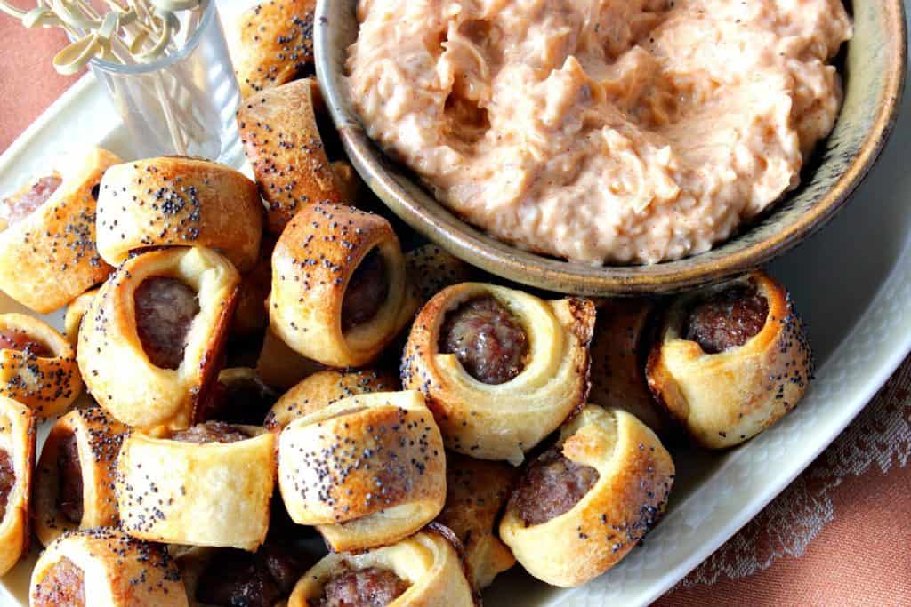 A horizontal photo of a plate of bratwurst appetizers with cocktail picks and a bowl of sauerkraut dipping sauce.