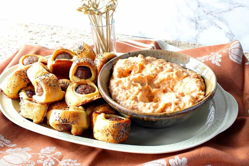 A horizontal photo of a plate of bratwurst appetizer bites with cocktail picks and a bowl of sauerkraut dipping sauce on a tan napkin.