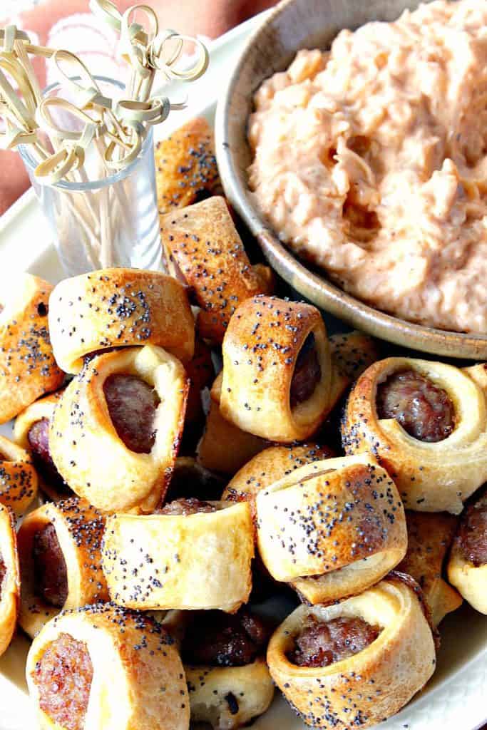 A vertical closeup image of bratwurst appetizer bites wrapped in dough and sprinkled with poppy seeds.