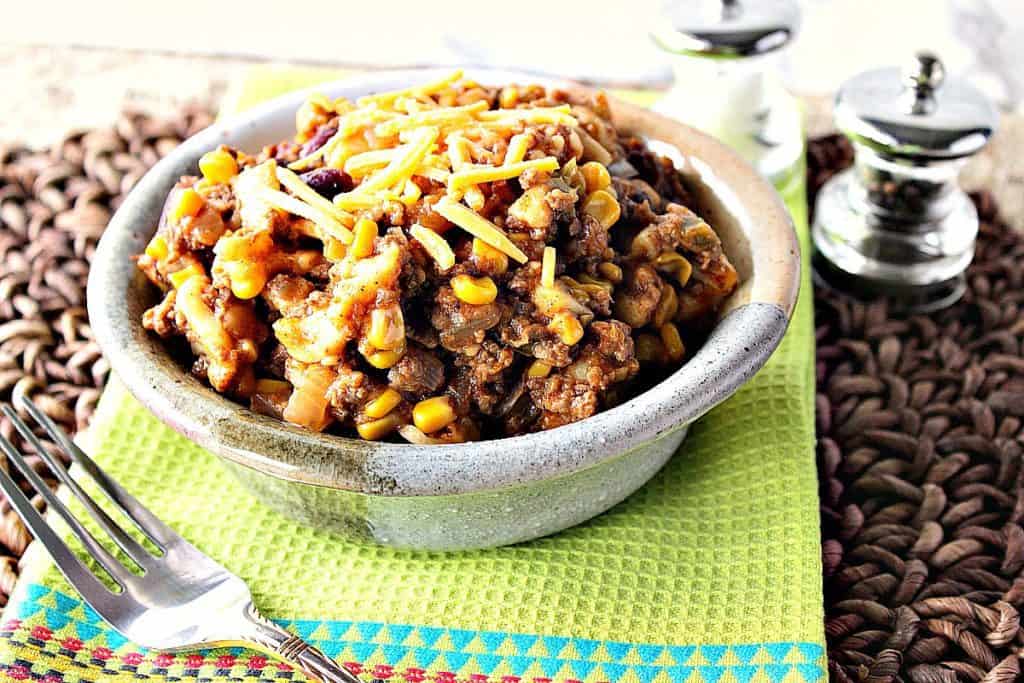 A pottery bowl filled with slow cooker chili mac topped with shredded cheese.